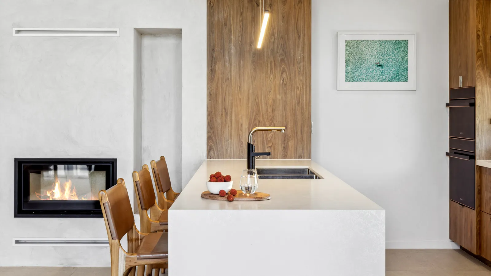 Modern kitchen with sleek white island, built-in fireplace, and warm wooden accent wall.