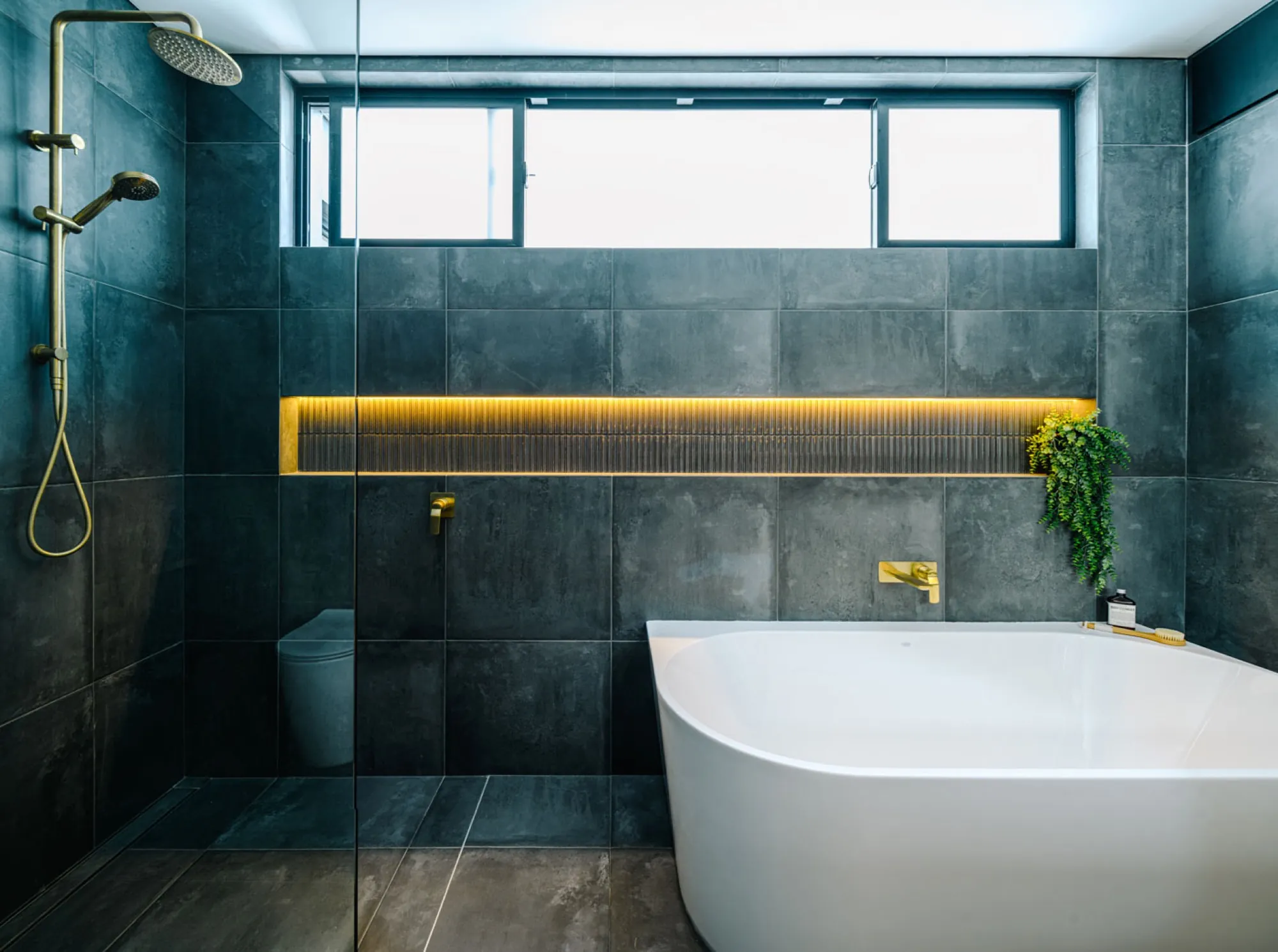 Modern luxury bathroom with freestanding bathtub, dark gray tiles, and gold accent lighting.
