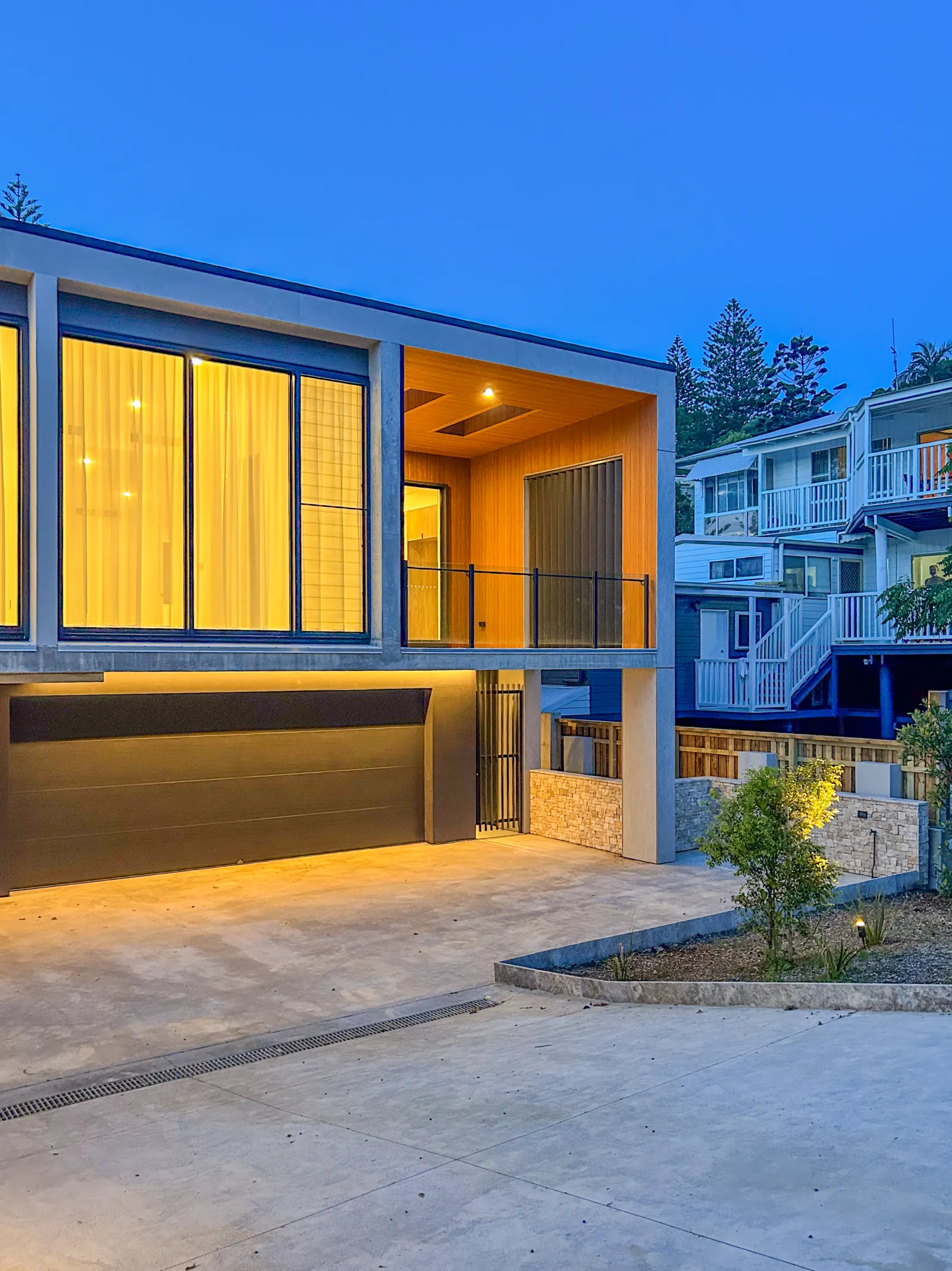Modern minimalist home with warm interior lighting and spacious concrete driveway.
