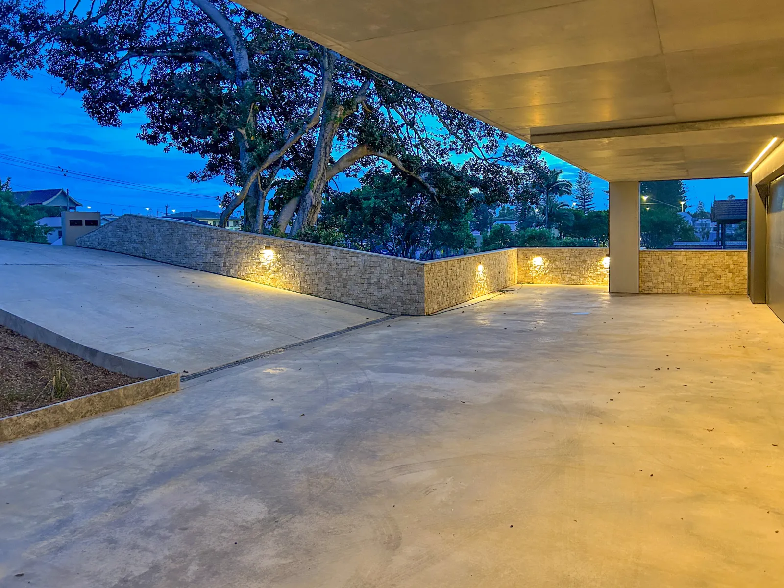 Modern outdoor living area with concrete floor, stone wall, and warm ambient lighting.